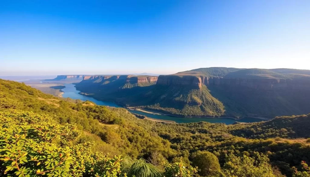 A sweeping landscape of Fazao-Malfakassa National Park, showcasing its distinct seasonal transformations. In the foreground, lush, verdant foliage covers the rolling hills, reflecting the vibrant greens of the wet season. In the middle distance, a winding river cuts through the landscape, its waters glimmering under the warm, golden sunlight. Beyond, the rugged, rocky cliffs rise up, capped with the soft pinks and purples of blossoming flowers during the spring. The sky is a serene, cloudless blue, casting a peaceful, calming atmosphere over the scene. Capture the park's natural beauty through a wide-angle lens, showcasing the diverse ecosystems and stunning vistas that visitors can expect to enjoy throughout the year.