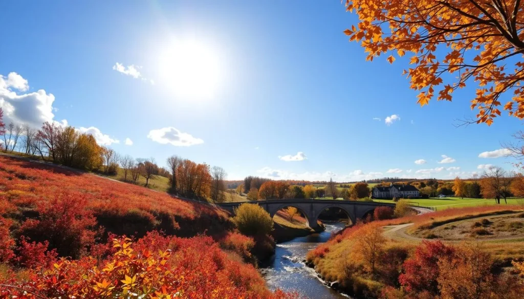 A sun-dappled autumn scene in Decorah, Iowa, showcasing the region's seasonal highlights. In the foreground, vibrant foliage in hues of red, orange, and gold blankets the rolling hills. A winding creek cuts through the landscape, its waters sparkling under the warm, golden light. In the middle ground, a historic stone bridge arches gracefully over the creek, while in the distance, the iconic Decorah Trout Hatchery and its lush green surroundings come into view. The sky is a serene azure, punctuated by fluffy white clouds. The overall mood is one of tranquility and natural beauty, capturing the essence of Decorah at its most picturesque.