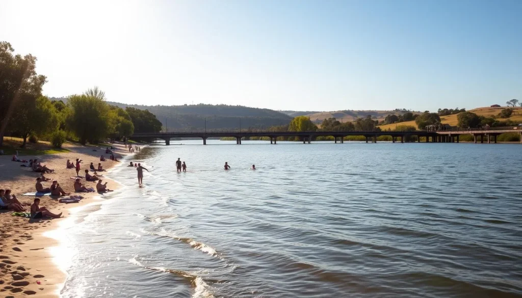 A tranquil riverside scene at Wagga Wagga Beach, New South Wales. Sunlight dances on the gently lapping waters of the Murrumbidgee River, with lush green trees lining the banks. In the foreground, families and friends relax on the sandy shores, some wading in the cool, refreshing shallows. In the middle ground, a picturesque wooden jetty extends into the river, inviting visitors to take in the serene vista. The background showcases the rolling hills and eucalyptus-covered landscape characteristic of the Riverina region. The scene exudes a sense of peaceful, laidback Australian charm on a picture-perfect day.